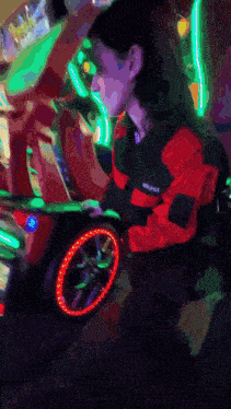 a woman in a red and black jacket is playing a video game in a dark room