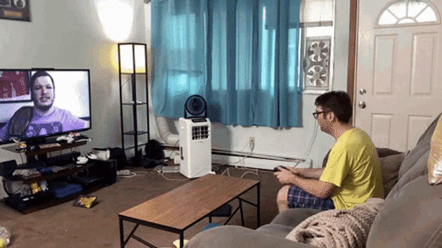 a man sitting on a couch playing a video game in front of a television
