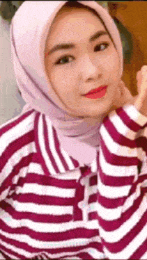 a woman wearing a hijab and a striped shirt is smiling for the camera .
