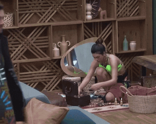 a woman in a neon green bikini sits on the floor looking at herself in a mirror