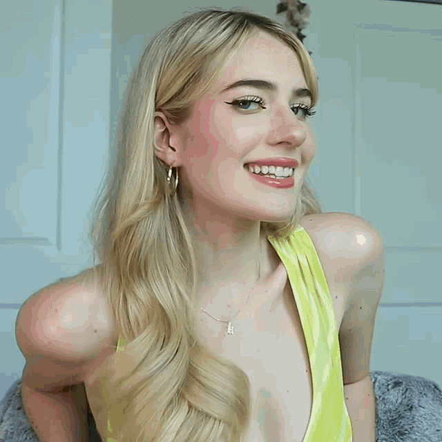 a woman wearing a yellow tank top and hoop earrings smiles