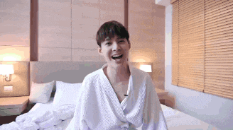 a young man wearing a white robe is sitting on a bed .
