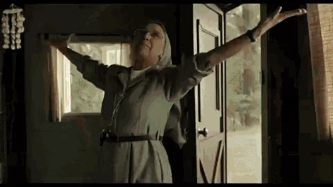 an elderly woman with her arms outstretched is standing in front of a door .