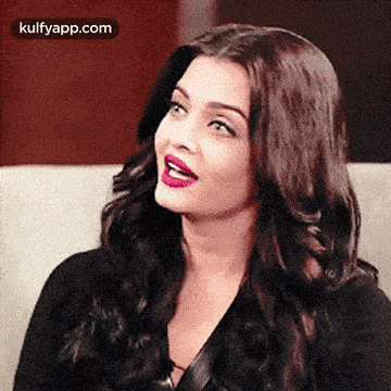 aishwarya rai is sitting on a couch with her mouth open and wearing a black top .