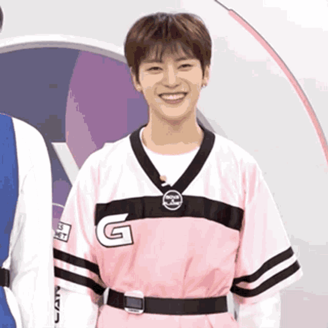 a young man in a pink and black jersey with the letter g on it is smiling .