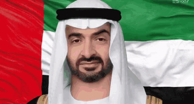 a man with a beard is standing in front of an arabic flag