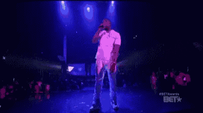 a man is dancing on a stage in front of a crowd while wearing a pink shirt .