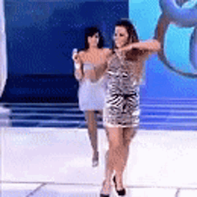a woman in a dress is dancing on a stage while another woman looks on .