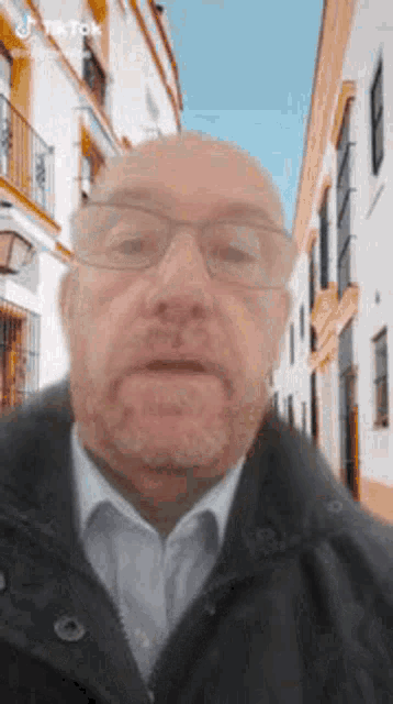 a man wearing glasses and a jacket is standing in front of a street .