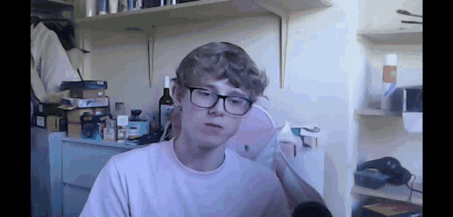 a young man wearing glasses and a pink shirt is sitting in a room