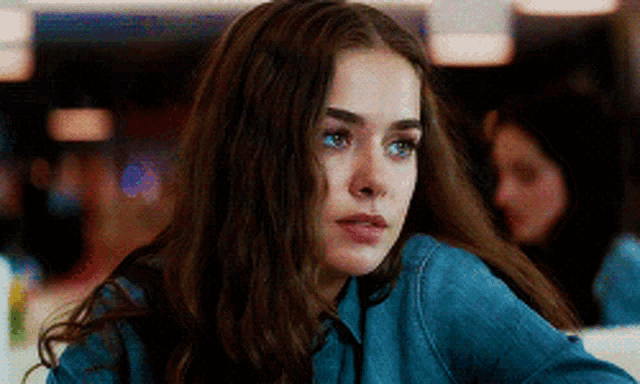 a woman with long hair is sitting at a table in a restaurant looking at the camera .