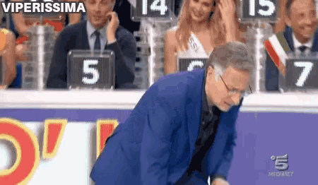 a man in a suit and glasses is standing in front of a sign that says viperissima
