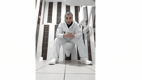 a man sits on a toilet in a bathroom with a striped wall behind him