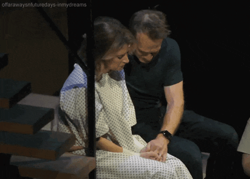 a woman in a hospital gown sits next to a man in a green shirt