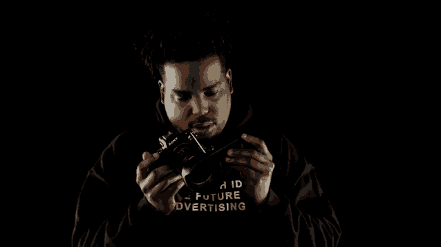 a man wearing a black hoodie that says hic future advertising holds a camera
