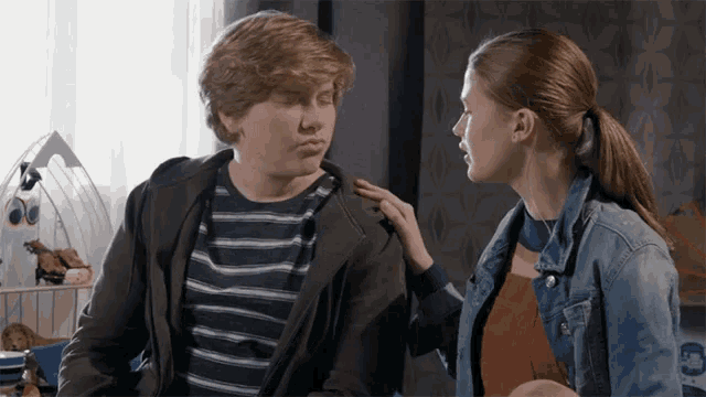 a girl in a denim jacket touches a boy 's shoulder