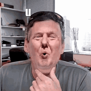 a man wearing sunglasses is making a funny face with the letter u above his head .
