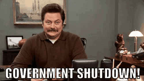 a man with a mustache is sitting at a desk with the words government shutdown written on the screen .