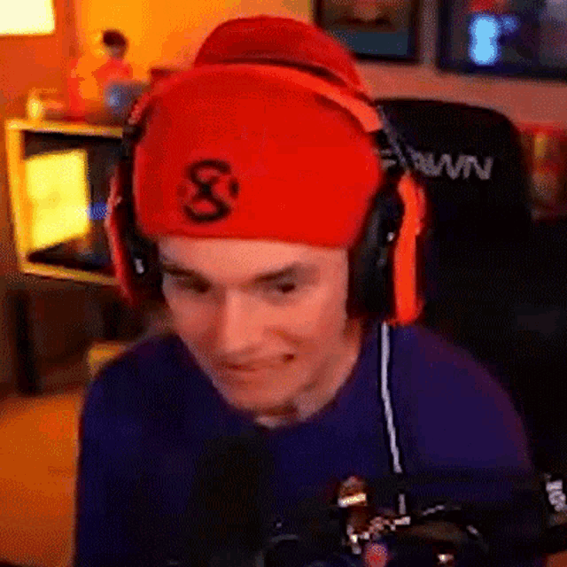 a man wearing headphones and a red hat is sitting in front of a microphone in a room .