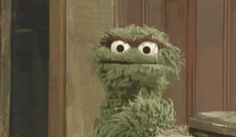 oscar the grouch from sesame street is making a funny face while standing next to a trash can .