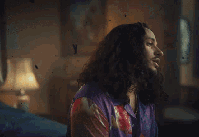 a man with long hair and a beard wears a purple shirt