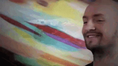 a man with a beard is smiling in front of a painting