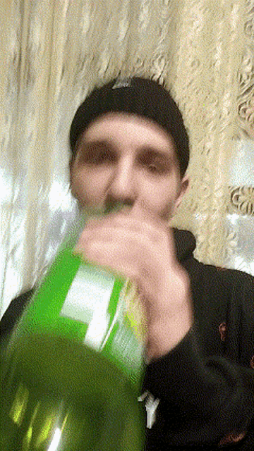a man is drinking from a green bottle with a white label