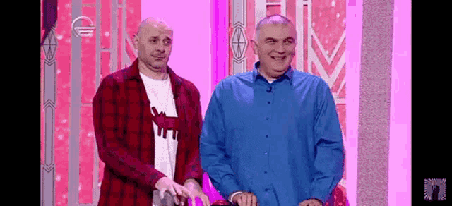 two men are standing next to each other on a stage and smiling . one of the men is wearing a plaid shirt .