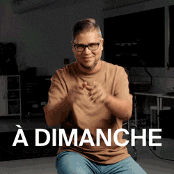 a man wearing glasses and a brown shirt is sitting in front of a sign that says a dimanche