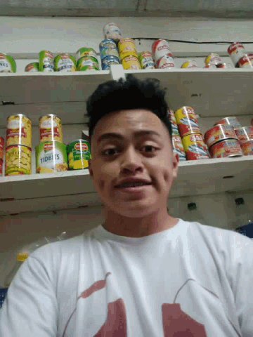 a man is standing in front of a shelf full of cans of food including a can of heinz tomato soup