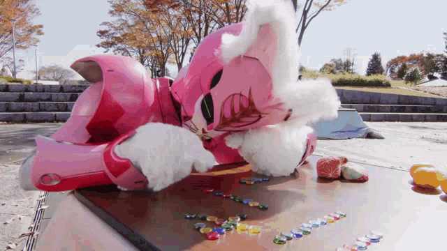 a pink robot is laying on a wooden table with a bunch of marbles on it