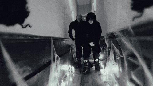 two men in masks are walking down a hallway with spider webs .