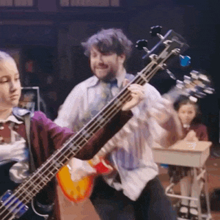 a man is playing a bass guitar in front of a group of children