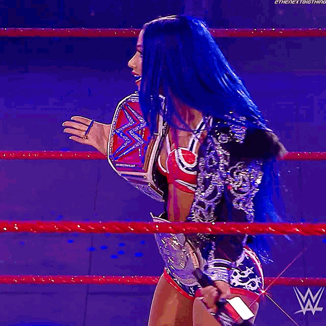 a woman with blue hair is in a wrestling ring holding a world heavyweight championship belt