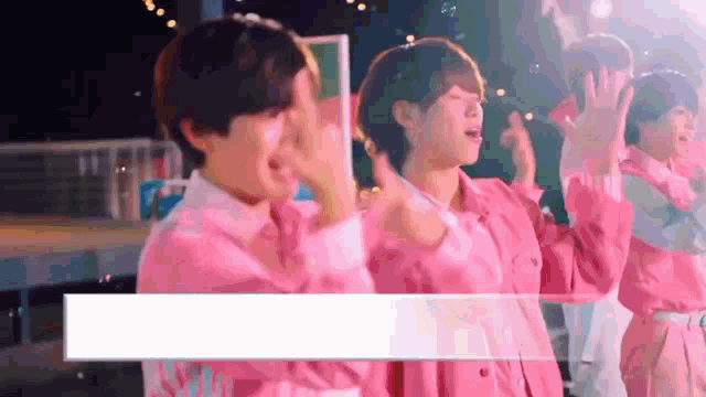 a group of young men wearing pink shirts are standing on a stage .