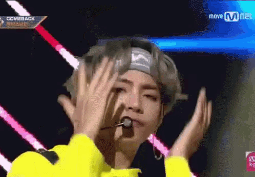 a man wearing a headband and a yellow shirt is making a funny face while holding his hands to his face .