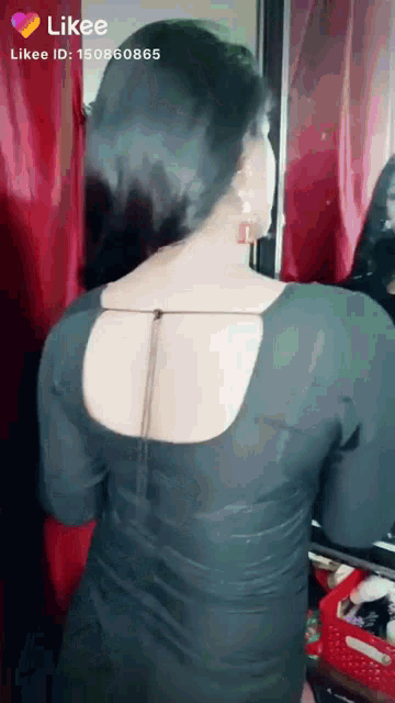 a woman in a black dress is standing in front of a mirror and looking at herself .