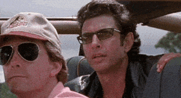 two men are sitting in a car and one has a hat that says jurassic park