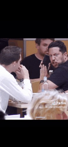 a group of men are sitting at a table with one man making a funny face .