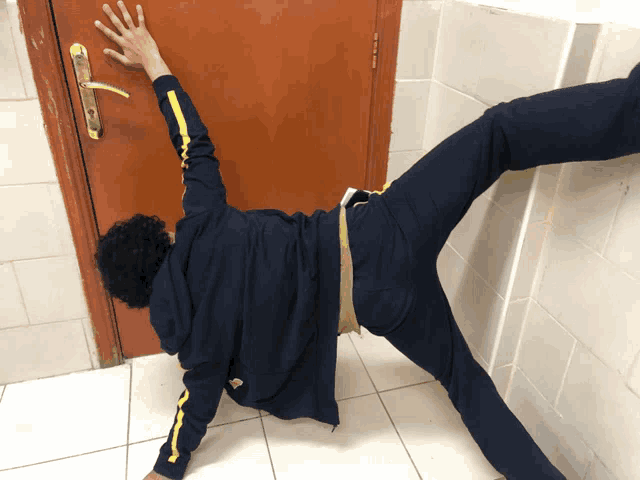 a person wearing a blue jacket with yellow stripes on the sleeves is reaching for a door