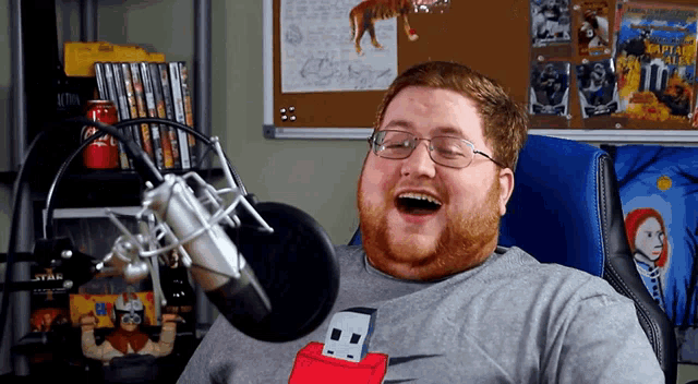 a bearded man wearing glasses and a nike flash drive shirt laughs in front of a microphone