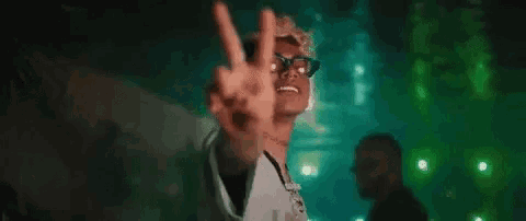 a man with glasses is making a peace sign with his hands in a dark room .