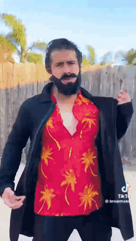 a man with a beard and mustache is wearing a red shirt and black coat .