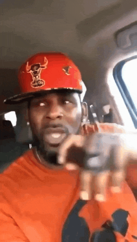 a man wearing a red hat and an orange shirt is in a car .