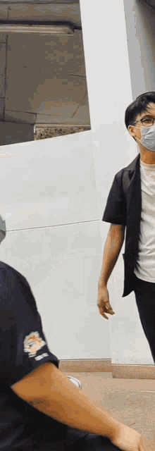 a man wearing a mask stands next to another man wearing a black shirt