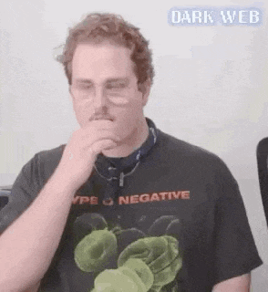 a man wearing glasses and a black t-shirt is covering his nose with his hand .