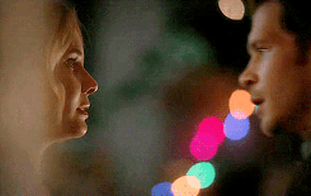a man and a woman are looking at each other in front of christmas lights .
