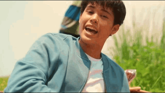 a young man wearing a blue jacket is sitting in the grass laughing .