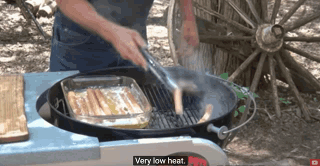 a man is cooking hot dogs on a grill with the words " very low heat " above him