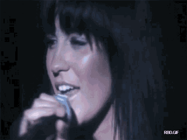 a close up of a woman singing into a microphone with rbd.gif written on the bottom